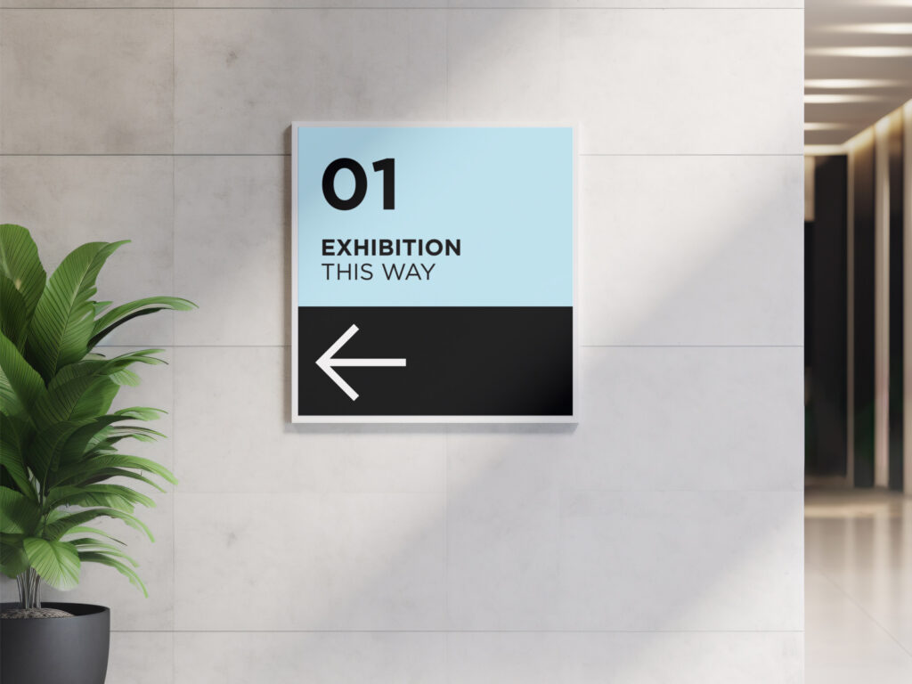 Wayfinding signage on a wall pointing left towards an exhibition